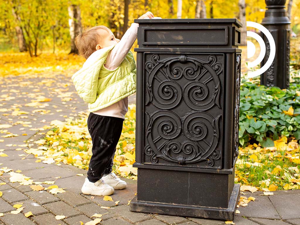 A child in a park throws trash in a cardboard basket that sends a signal when emptying needs